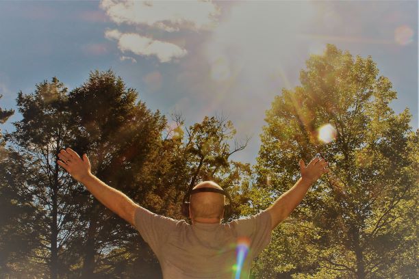 man physically energized by music, arms in the air on a beautiful, sunny day